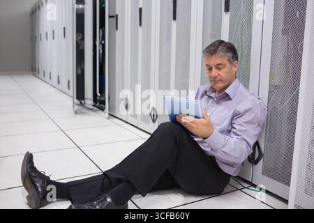 Senior man in dress clothes leaning against server rack, checking tablet at data center, copy space Stock Photo