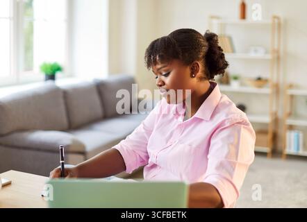 Serious african american business woman working on a laptop and making notes in office. Stock Photo
