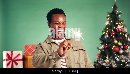 Christmas, laugh and black man with sparkler in studio for festive season on green background. African person, xmas and firework for holiday Stock Photo