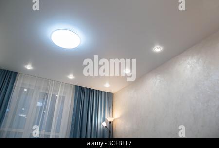 Modern stylish ceiling with diode chandelier and spotlights in the room and turquoise curtains Stock Photo