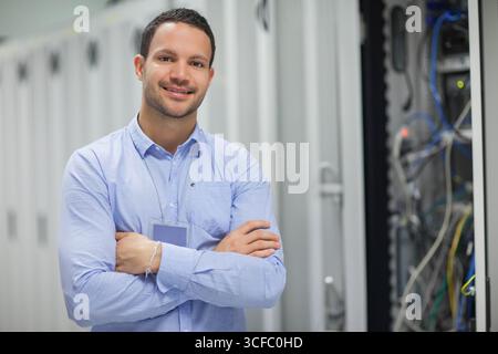 Male IT technician standing with arms crossed in data center server cabinets and cables, copy space Stock Photo