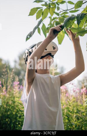 Man child in virtual reality glasses touches leaves Stock Photo