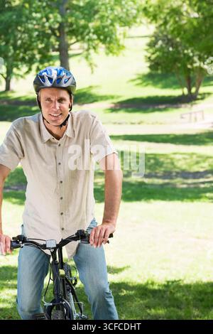 Middle-aged man wearing bicycle helmet sitting on bicycle in park monitoring cycle computer Stock Photo