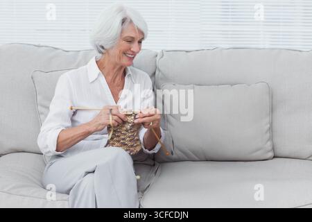 Wooden knitting needles combining brown and beige yarn on light grey sofa near white blinds Stock Photo