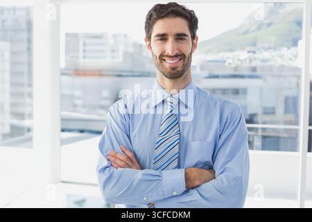 Businessman posing with arms crossed wearing striped tie in office with floor-to-ceiling windows Stock Photo
