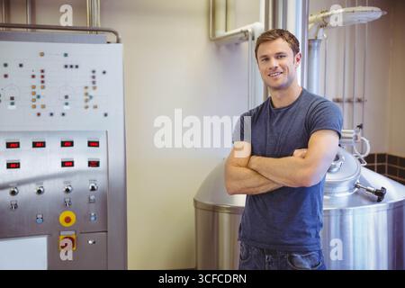 Technician is standing next to stainless steel fermentation tank and control panel in brewery room Stock Photo