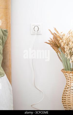White plug in socket with cable hanging. Power connection for electrical appliances. Utility and energy supply for home interior. Stock Photo