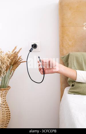 Woman holding charger cable with plug in the socket. Hand putting cable into electrical outlet. Stock Photo
