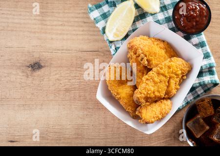 Close-up of golden crispy fried chicken tenders served in a red and white paper tray on wooden table. Stock Photo