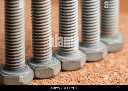Shiny metallic bolts lined neatly on a textured wooden surface, showcasing detail. Stock Photo