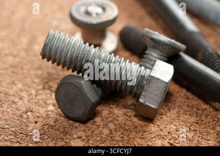 Close-up view of various metal fasteners resting on a beige cork surface. Stock Photo