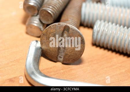 Close-up of a rusty bolt surrounded by assorted screws on a wooden surface. Stock Photo