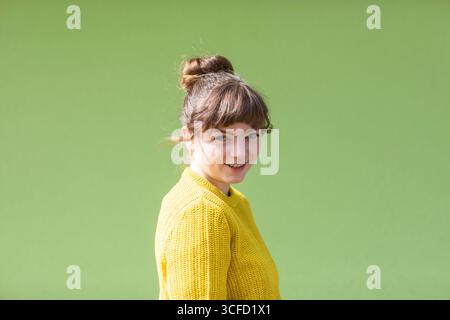 Young woman in yellow sweater smiles in front of a bright green background. Germany Stock Photo