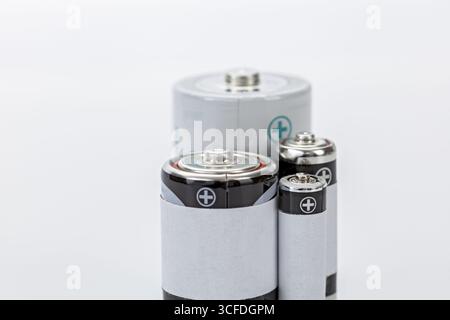 A various size batteries with metallic tops and white labels, arranged on white background, showing positive terminals and clean, minimal design Stock Photo