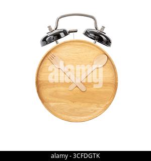 A wooden plate with fork and spoon arranged as clock hands, metal alarm clock bells on top, creative concept for meal time, isolated on white Stock Photo