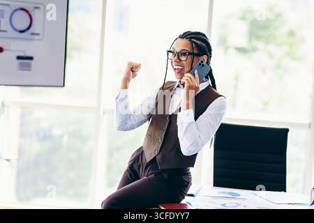 Young businesswoman celebrates success while talking on the phone in a modern office setting Stock Photo
