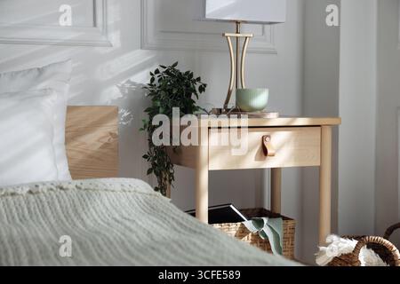 Bedside table with lamp and other decor near bed indoors Stock Photo