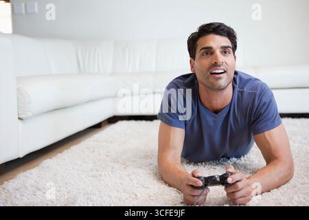 Mid adult man lying in living room on white shag rug holding black controller, copy space Stock Photo