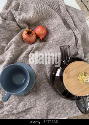 Empty tea cup, teapot and two pomegranates on warm sweater. Cozy autumn mood and relaxation concept. Top view, flat lay. Autumn composition. Stock Photo