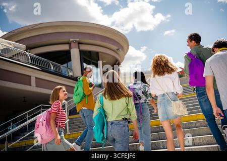 Students enjoying a sunny day together walking up stairs to a modern building carrying backpacks Stock Photo