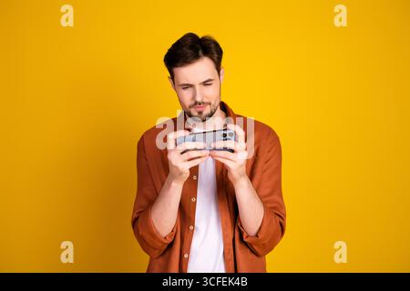 Handsome man in casual attire engrossed with a smartphone against a vibrant yellow background expressing style and modern lifestyle Stock Photo