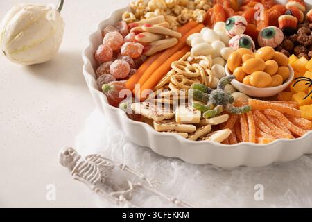 Halloween charcuterie board with pumpkin color chocolate candy, spider, crackers on white background. Close up. Stock Photo