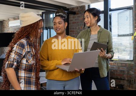 Diverse female coworkers collaborating while reviewing data on laptop and tablet in loft office Stock Photo