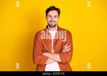 Handsome man in a casual outfit standing confidently against a vibrant yellow background, crossing his arms and smiling warmly Stock Photo