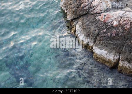 Turquoise seawater and rocky coastline with underwater stones visible. Natural marine background. Stock Photo