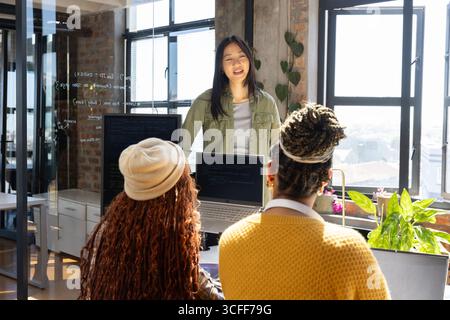 Diverse female coworkers collaborating on whiteboard code with laptops, potted plants in office Stock Photo