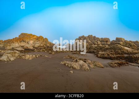 A close-up of large rock formations and tide pools on the shore of Matanzas, Chile, under a misty, dramatic sky. Stock Photo