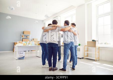 Group of volunteers standing together in circle and hugging during work in humanitarian center. Stock Photo