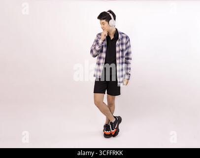 young man standing with headphones and smiling against plain background Stock Photo