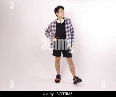young man standing with headphones and smiling against plain background Stock Photo