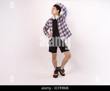 young man standing with headphones and smiling against plain background Stock Photo