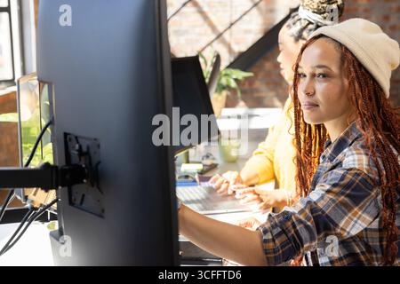 Diverse coworkers adjusting monitor and typing on laptop at desk in open plan office, copy space Stock Photo