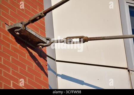 Turnbuckle and threaded rods tensioning device attached to brick wall anchor point. Stock Photo