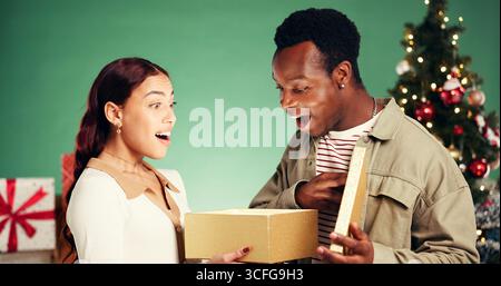 Christmas, gift and shocked with interracial couple in studio for holiday season, celebration and xmas. Present, festive tradition and man with woman Stock Photo