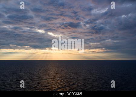 Dramatic cloudy sky over calm sea at golden hour with sunlight breaking through clouds Stock Photo
