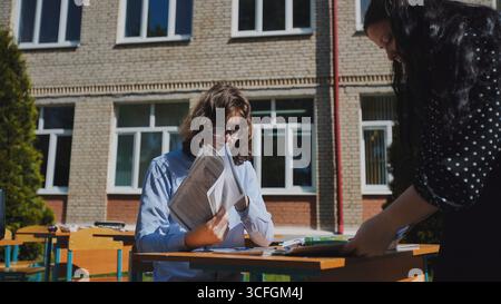 Two high school students collaborating on a project outdoors, embracing the sunshine and fresh air at their school Stock Photo