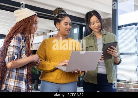 Diverse female colleagues collaborating on project using laptop and tablet in modern office Stock Photo