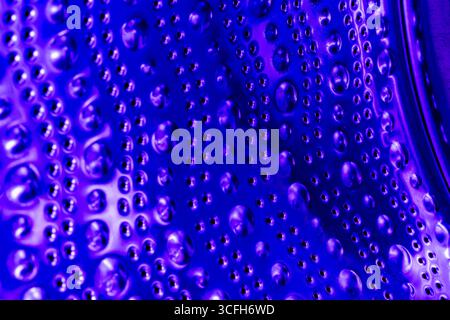 Empty washing machine drum inside in blue light, close up view. Metal dots and bubbles as abstraction and background Stock Photo