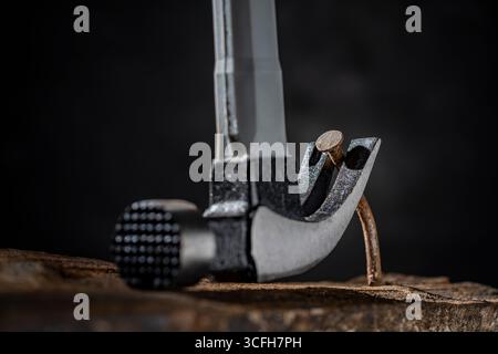 Using a hammer to pull out an old rusty nail from a wooden board on a dark background in the workshop, close up. Hand tool for working Stock Photo