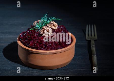 Beetroot salad with walnuts and green dill in a bowl on wooden table background, close up. Grated boiled red beetroot in a clay bowl. Dieting and vege Stock Photo