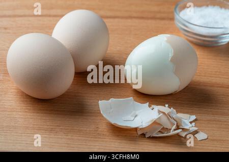 Fresh hard boiled three eggs with shell and salt on wooden board, close up Stock Photo