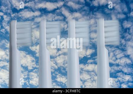 Four white plastic toothbrushes on a blue sky background, close up Stock Photo