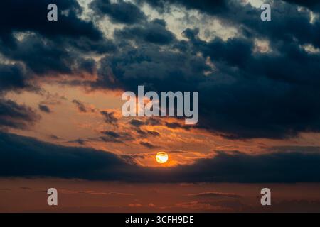 Dark dramatic horizon sky during sunset. Black clouds and setting sun. Evening sunshine background Stock Photo