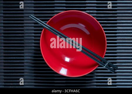 A pair of black chopsticks lying across an empty red soup bowl on wooden striped tray, close up, top view Stock Photo