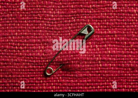 Gold toned safety pin on red fabric background, close up. Metal pin in rough textile fabric closed, macro Stock Photo
