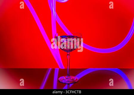 Glass goblet filled with drink and ice cubes on reflective surface against red background. Sweden. Stock Photo